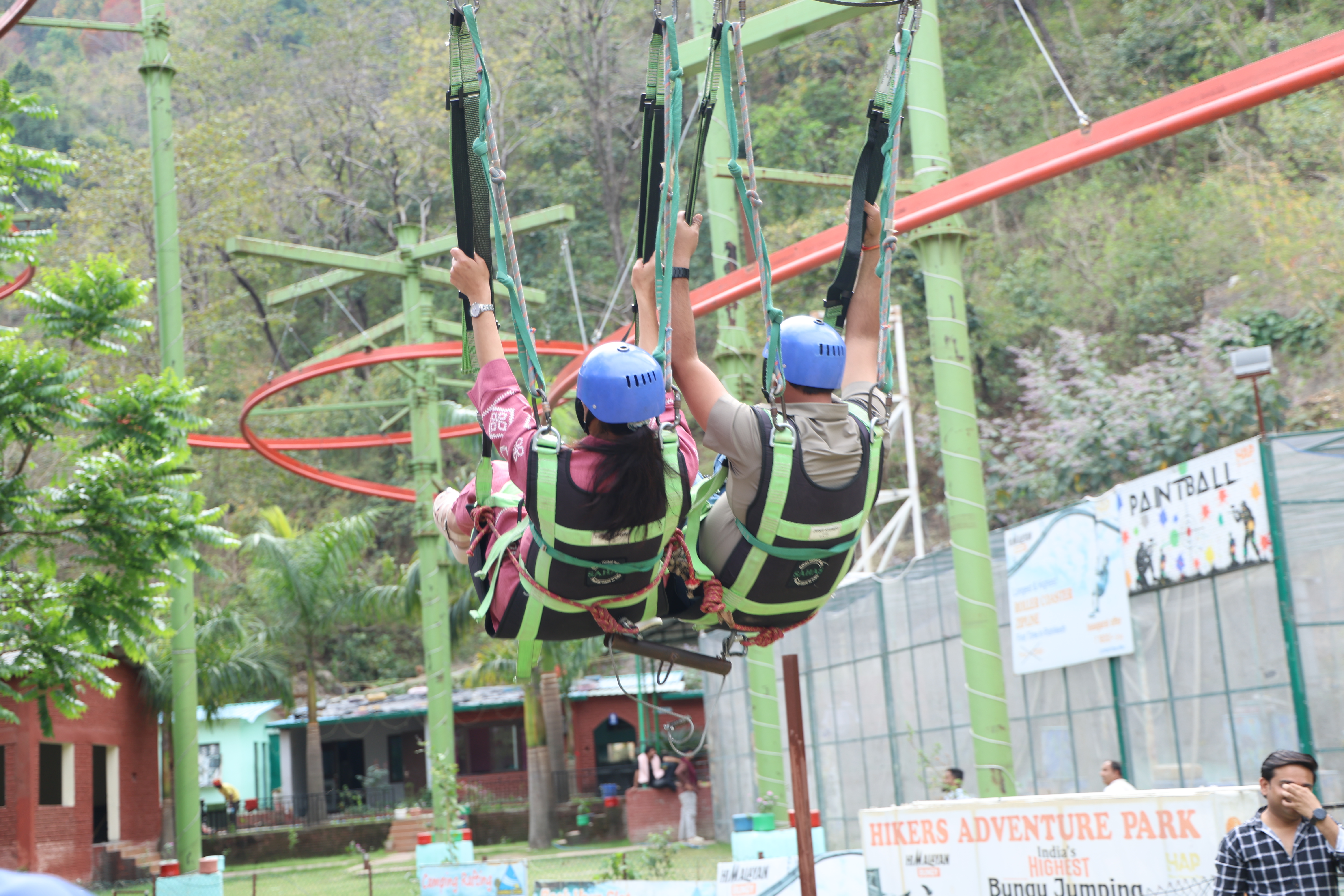 Giant swing experience in Rishikesh with two participants wearing safety helmets and harnesses at an adventure park.