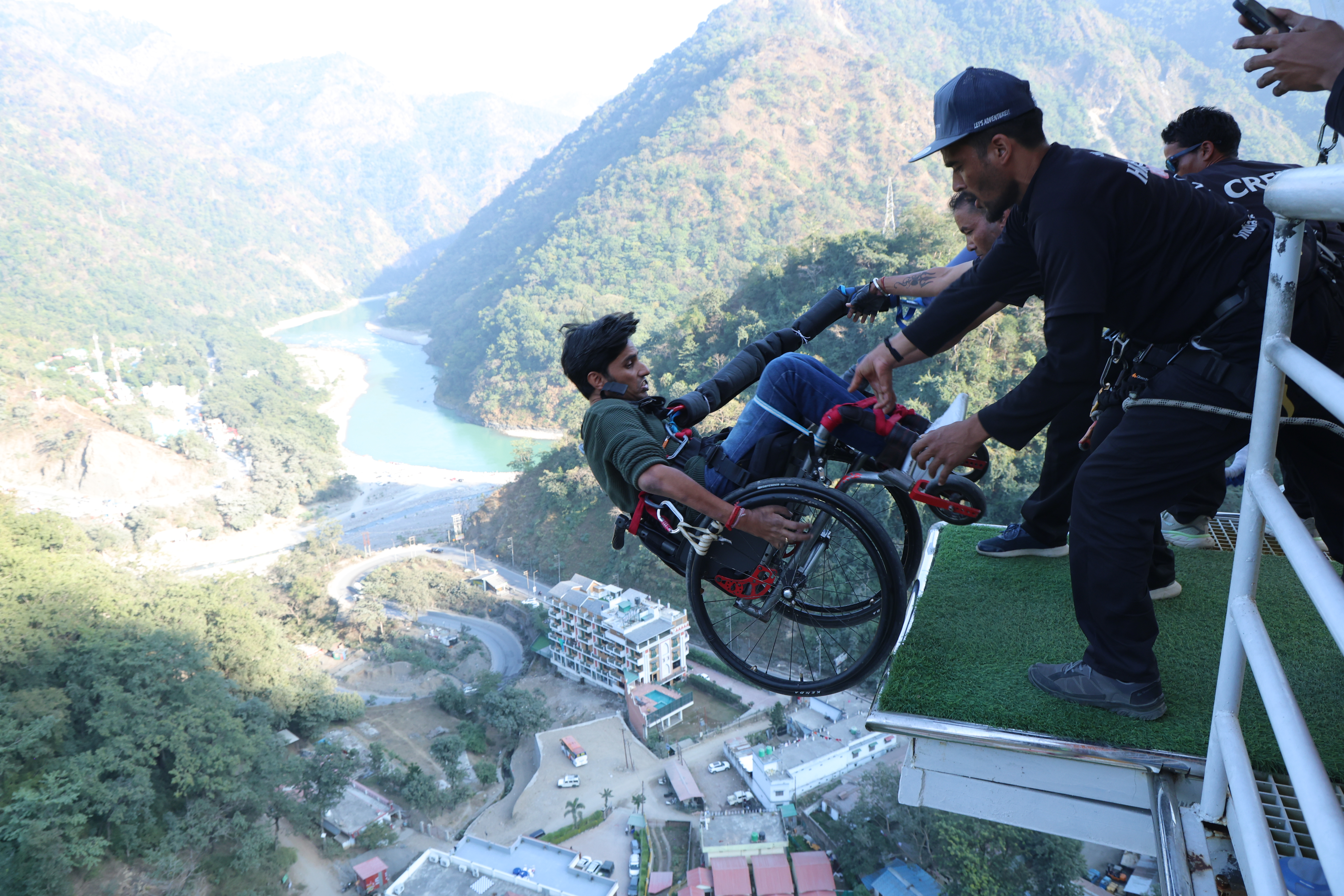 Wheelchair user preparing for an assisted bungee jump at an adventure platform in Rishikesh, surrounded by green hills and the Ganga valley.